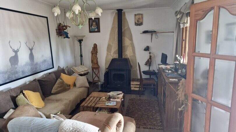 Wohnzimmer der Finca mit Kaminofen, Natursteinwand, Sofa und rustikalem Holzcouchtisch