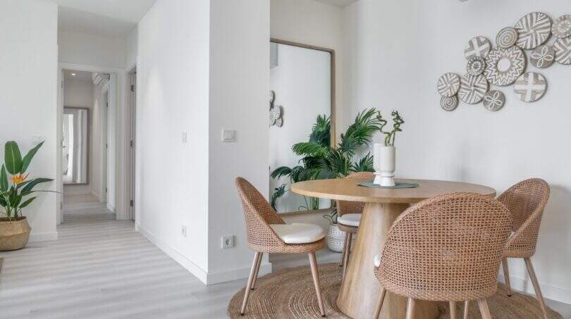 Área de comedor luminosa con sillas de ratán, mesa de madera y decoración de pared en apartamento exclusivo en Palma de Mallorca.