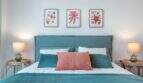 Dormitorio elegante con cama doble turquesa, cojines de coral y obras de arte marinas en apartamento en Palma
