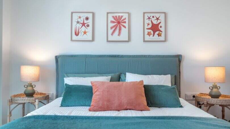 Dormitorio elegante con cama doble turquesa, cojines de coral y obras de arte marinas en apartamento en Palma