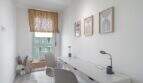 Despacho luminoso con escritorio blanco, sillas grises, estor de bambú e imágenes de pared modernas en apartamento en Palma.