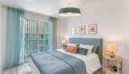 Dormitorio luminoso del apartamento en Palma con cama azul, cortinas en la puerta y acceso al balcón