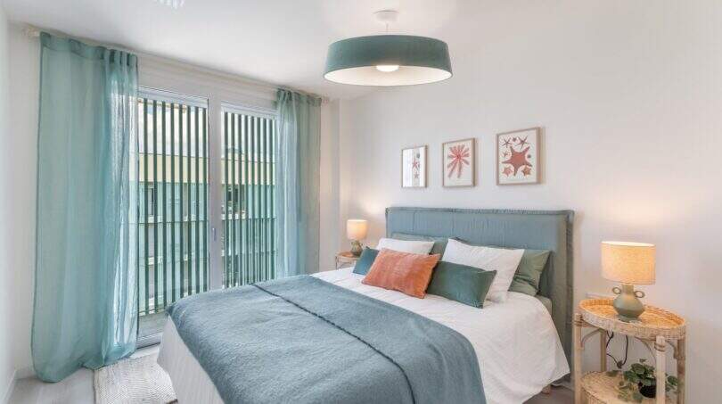 Dormitorio luminoso del apartamento en Palma con cama azul, cortinas en la puerta y acceso al balcón