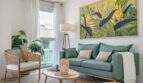 Sala de estar luminosa con sofá verde, pintura tropical y materiales naturales en apartamento exclusivo en Palma.