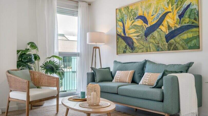 Sala de estar luminosa con sofá verde, pintura tropical y materiales naturales en apartamento exclusivo en Palma.