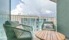 Balcón del apartamento exclusivo en Palma con sillas de ratán verdes, mesa de madera y vista de edificios adyacentes