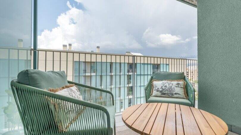 Balcón del apartamento exclusivo en Palma con sillas de ratán verdes, mesa de madera y vista de edificios adyacentes