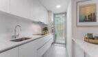 Cocina tipo galera blanca moderna con electrodomésticos empotrados y acceso al balcón en apartamento exclusivo en Palma de Mallorca