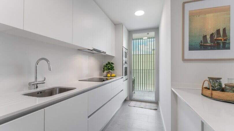 Cocina tipo galera blanca moderna con electrodomésticos empotrados y acceso al balcón en apartamento exclusivo en Palma de Mallorca