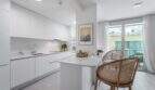 Cocina blanca moderna con isla de cocción, sillas de ratán y acceso a la terraza en apartamento exclusivo, Palma de Mallorca.