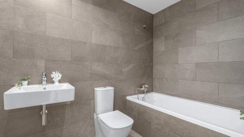 Baño moderno con azulejos con óptica de piedra gris, bañera empotrada, WC y lavabo montado en la pared en apartamento en Palma