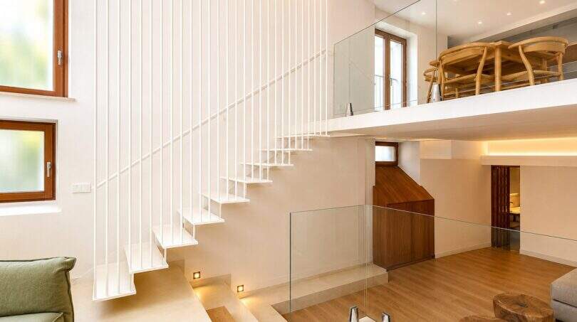 Modernes Duplex in Palma: Schwebende weiße Treppe mit Glasgeländer, Mezzanine-Ebene und Holzboden