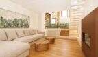 Helles Wohnzimmer mit Leinensofa, Naturholz-Couchtischen, Kaktus-Kunstwerk und Treppe zum Obergeschoss