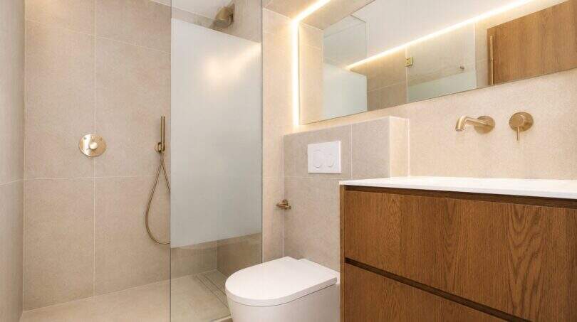 Modernes Designerbad mit Walk-in-Dusche, Wand-WC, Holzwaschtisch und goldenen Armaturen im Duplex Palma