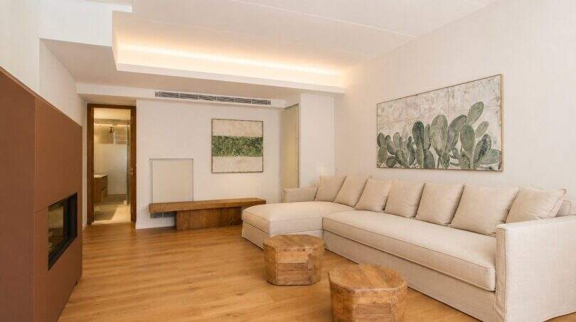 Helles Wohnzimmer mit cremefarbenem L-Sofa, Holzboden, Kaktus-Kunstwerk und modernem Kamin im Designer-Duplex Palma