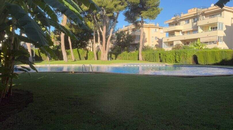 Piscina comunitaria con césped bien mantenido y jardín del complejo de áticos en Llucmajor, Mallorca.