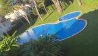 Piscina comunitaria con forma de riñón con césped bien mantenido y pinos junto al ático en Llucmajor
