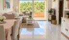 Sala de estar luminosa con piso de mármol, balcón y vistas a bosques de pinos en el ático de Mallorca