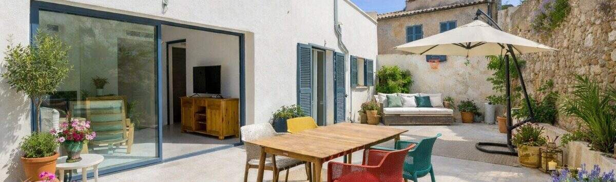 Sonnige Terrasse mit bunten Stühlen, Holztisch und Loungebereich beim Stadthaus in Artà