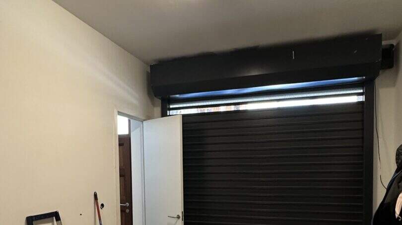 Garage mit schwarzem Rolltor, Seiteneingang, Deckenleuchte und Abstellfläche für Fahrräder in Artà.