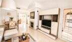 Helles Wohnzimmer der Doppelhaushälfte in Llucmajor mit TV-Wand, Kamin und Essbereich in Beige-Tönen.