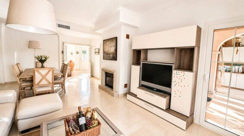 Helles Wohnzimmer der Doppelhaushälfte in Llucmajor mit TV-Wand, Kamin und Essbereich in Beige-Tönen.