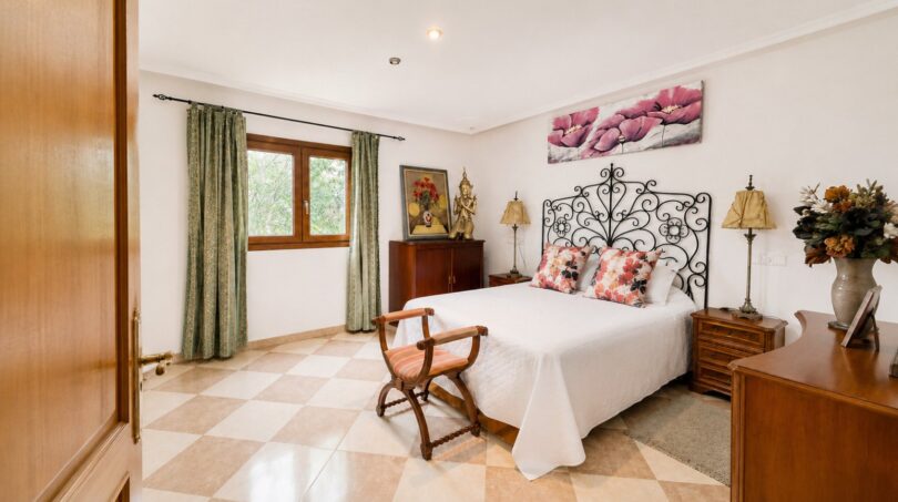Schlafzimmer der Finca Llucmajor mit schmiedeeisernem Bett, Fliesenboden & grünen Vorhängen