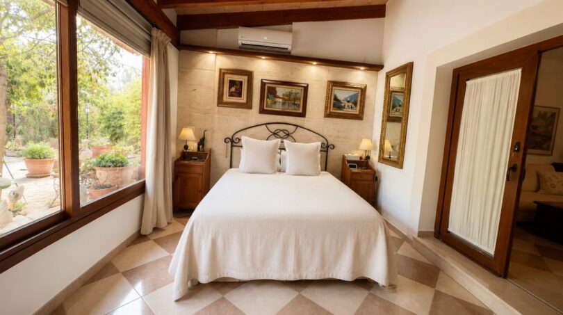 Elegantes Schlafzimmer der Finca Llucmajor mit Doppelbett, Holzbalken, Gemälden & Gartenblick