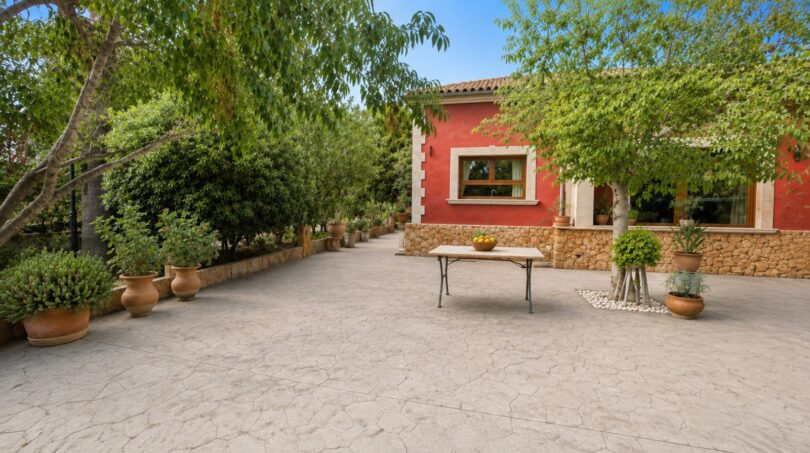 Gepflasterter Innenhof der Finca in Llucmajor mit roter Fassade, Natursteinmauer und mediterranen Terrakottatöpfen.