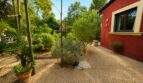 Kiesweg neben rotem Ferienhaus der Finca in Llucmajor mit mediterranem Garten und üppigem Grün