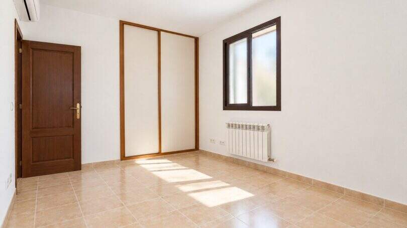 Leeres Schlafzimmer mit Fliesenboden, Einbauschrank, Fenster und Heizkörper im Wohnhaus in Establiments