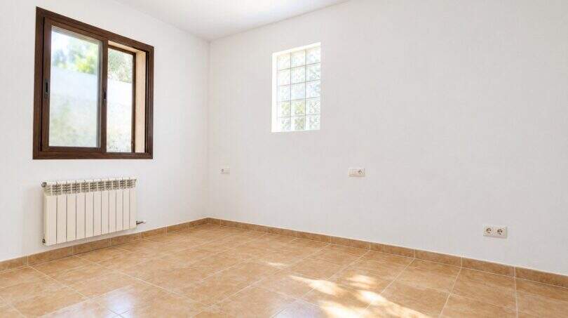 Leeres Schlafzimmer mit Terrakottafliesen, Heizkörper und zwei Fenstern im Wohnhaus in Establiments, Mallorca.