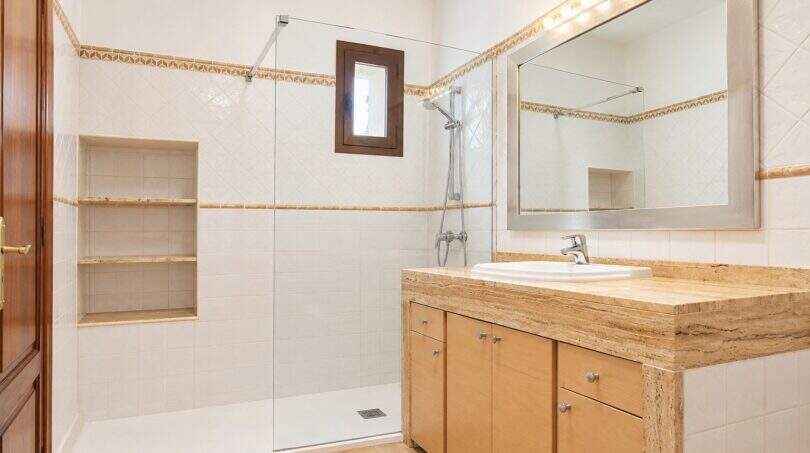 Helles Badezimmer mit Glasdusche, Marmor-Waschtisch und Holzunterschrank im Wohnhaus in Establiments, Mallorca.