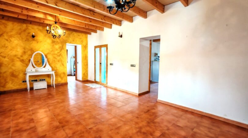 Amplio salón de la finca Inca con suelo de terracota, techo de vigas de madera y acento de pared amarillo