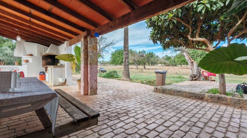 Terraza cubierta con adoquines, zona de barbacoa y vistas al jardín de la finca cerca de Inca