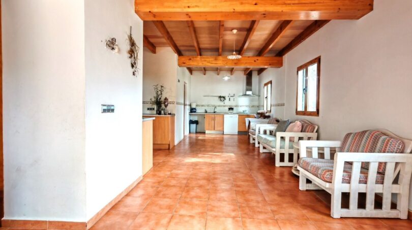 Área de salón-cocina abierta de la finca cerca de Inca con techo de vigas de madera, muebles blancos y suelo de terracota
