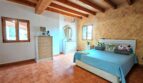 Dormitorio luminoso de la finca Inca con techo de vigas de madera, suelo de terracota y ropa de cama de color turquesa