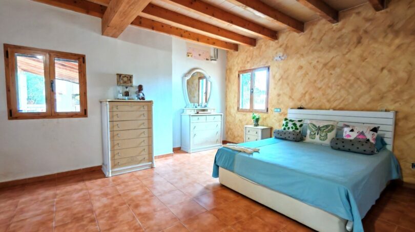 Dormitorio luminoso de la finca Inca con techo de vigas de madera, suelo de terracota y ropa de cama de color turquesa