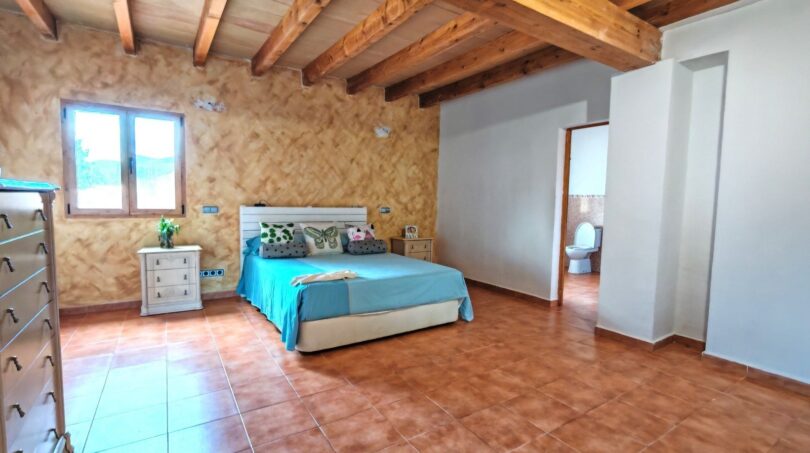 Amplio dormitorio de la finca Inca con techo de vigas de madera, suelo de terracota y baño privado
