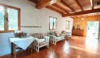 Salón luminoso de la finca Inca con techo de vigas de madera, muebles de estar blancos y suelo de terracota