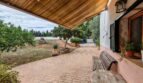 Terraza cubierta de la finca cerca de Inca con banco de madera, adoquines de barro y exuberante jardín con árboles frutales