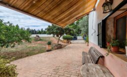 Überdachte Terrasse der Finca bei Inca mit Holzbank, Ziegelpflaster und üppigem Garten mit Obstbäumen