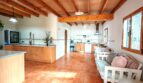 Amplia sala de estar-cocina de la finca cerca de Inca con techo de vigas de madera, suelo de terracota y muebles de estar blancos