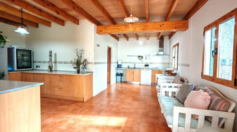 Amplia sala de estar-cocina de la finca cerca de Inca con techo de vigas de madera, suelo de terracota y muebles de estar blancos