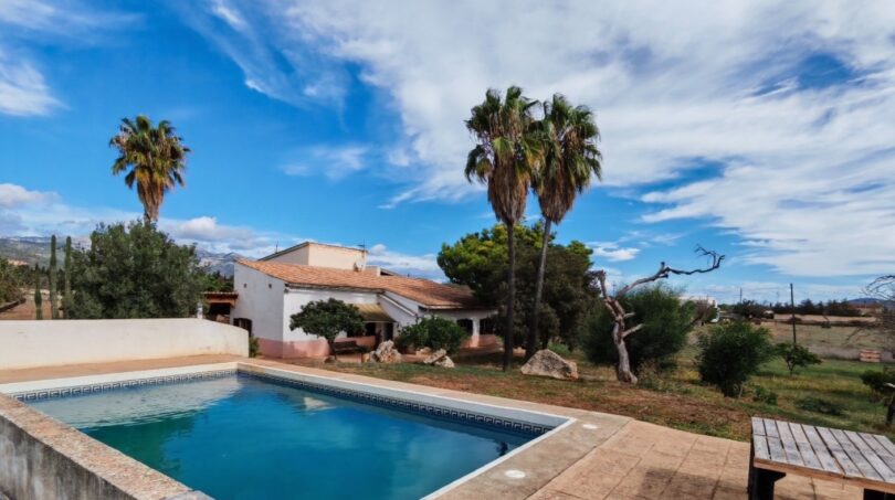 Finca Inca: Piscina exterior con azulejos de terracota, villa blanca, palmeras y vistas de la sierra de Tramuntana bajo cielo azul