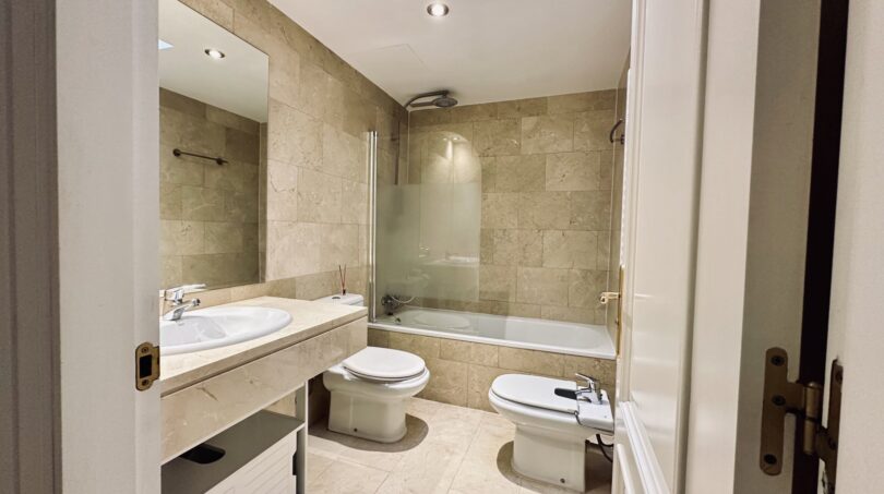 Elegante baño con azulejos de mármol, bañera con ducha, lavabo, WC y bidé en apartamento La Bonanova