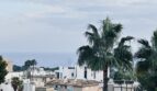 Vista desde la terraza en La Bonanova sobre casas blancas, palmeras y el Mediterráneo bajo cielo nublado.