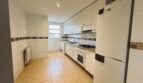 Luminosa cocina del apartamento en La Bonanova con armarios empotrados blancos, estufa de gas, nevera y suelo de azulejos.