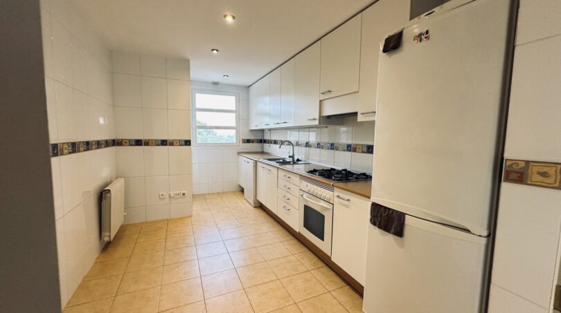 Luminosa cocina del apartamento en La Bonanova con armarios empotrados blancos, estufa de gas, nevera y suelo de azulejos.
