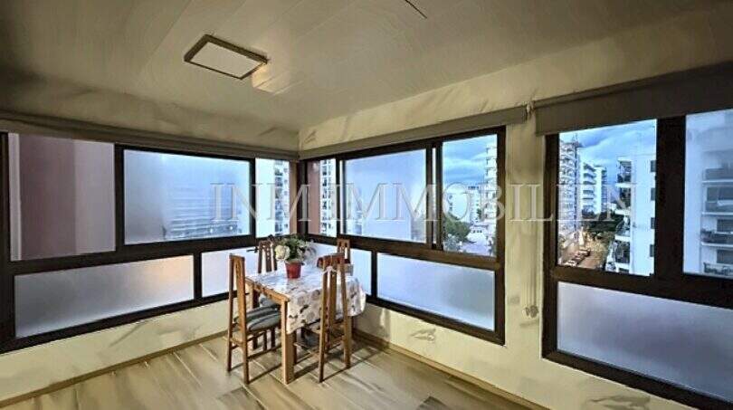 Verglaster Balkon mit Esstisch, Holzboden und Panoramablick auf Gebäude in El Arenal, Palma de Mallorca.